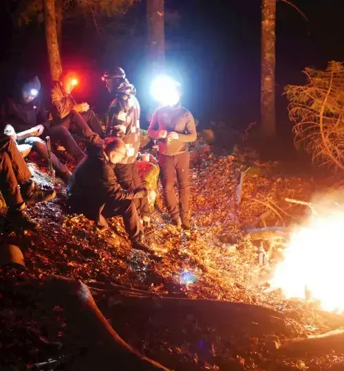 Deelnemers bij kampvuur met hoofdlampen tijdens bezinningsmoment van MTA 3-daagse Vogezen